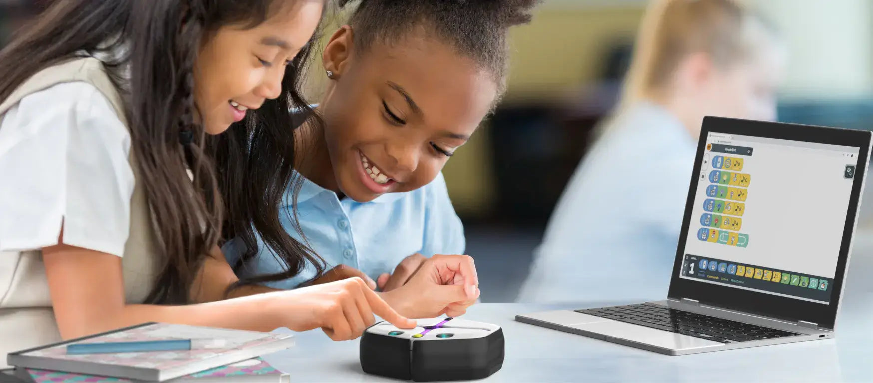 Two young girls engaging with the Root coding robot and laptop, enhancing their coding skills together.