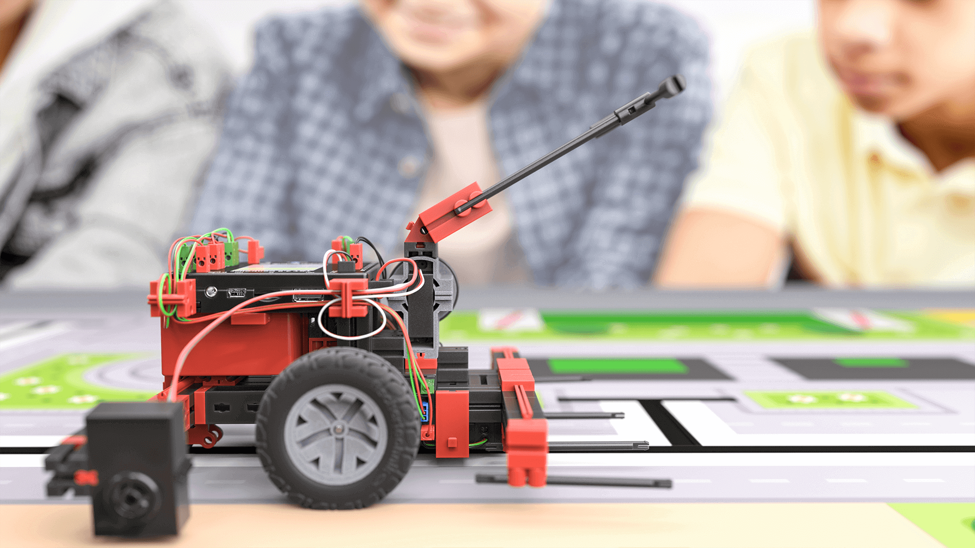 Robotic vehicle on a play mat with children engaged in STEM education activities in the background.
