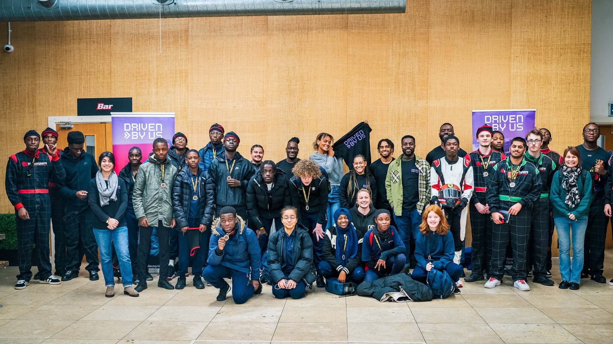 Group photo of diverse individuals in front of a 'Driven By Us' banner, showcasing community and collaboration.