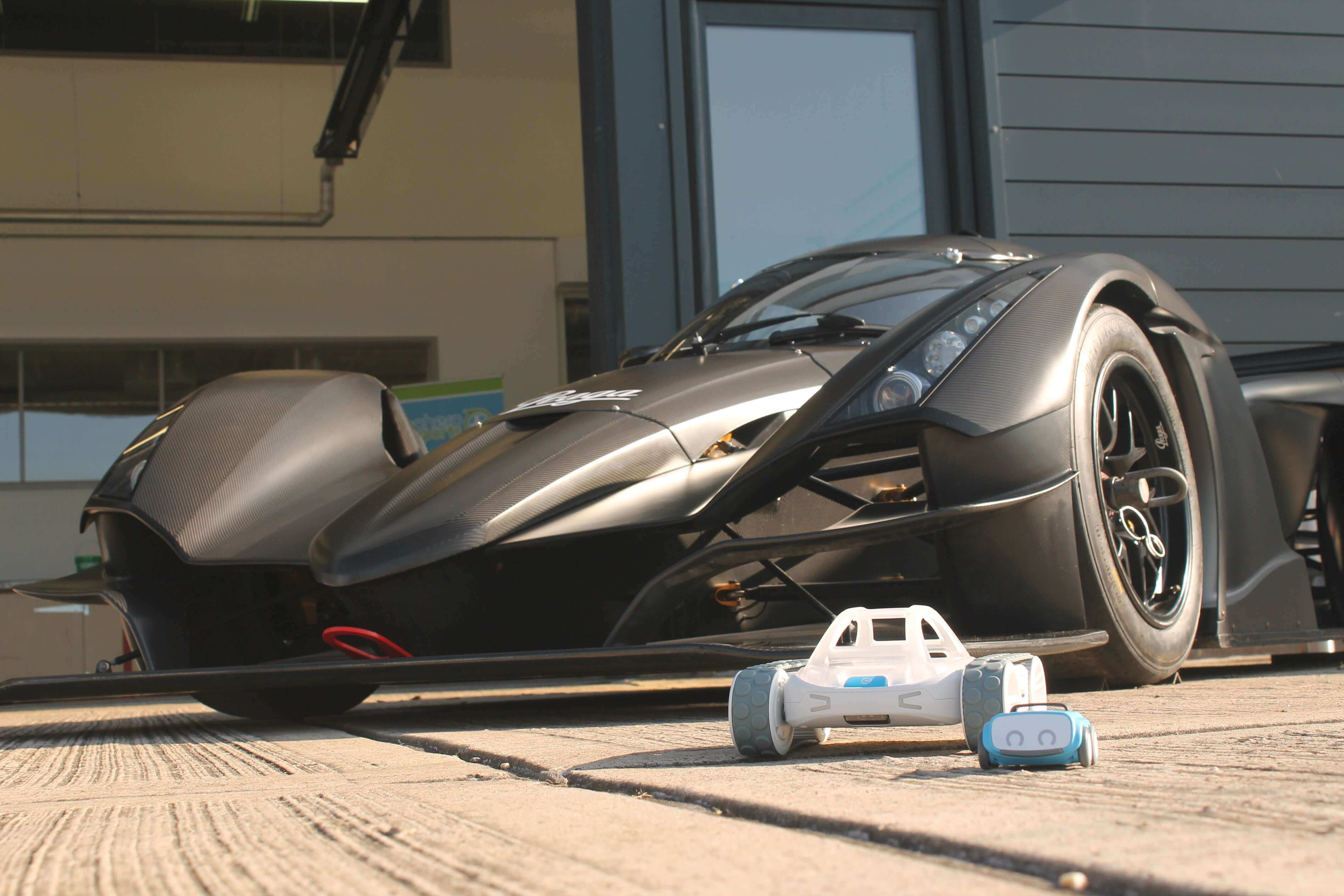 Sleek black sports car with a miniature toy car in front, showcasing scale and design contrast.