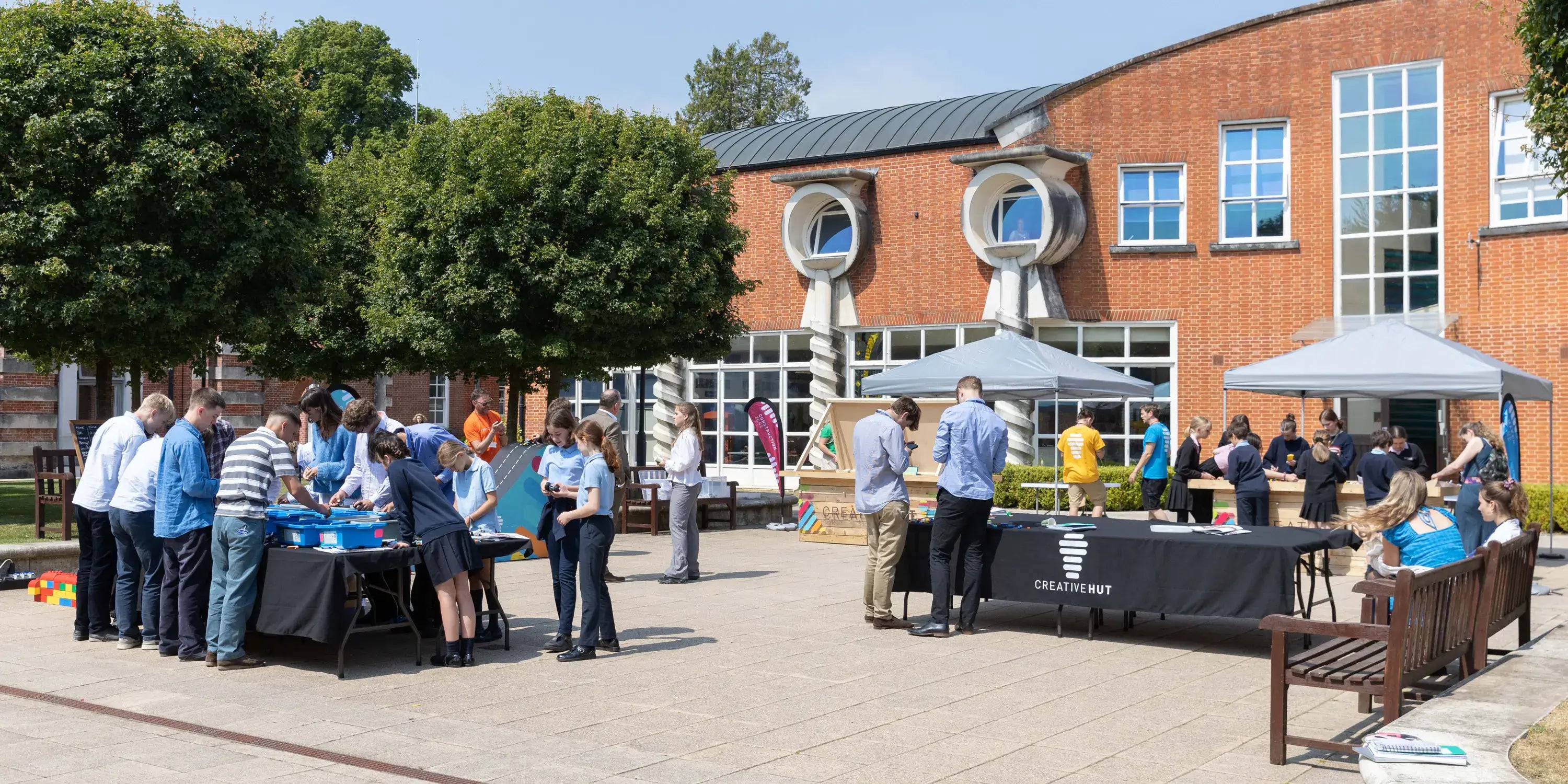 Outdoor community event with people interacting and booths set up in a sunny courtyard.