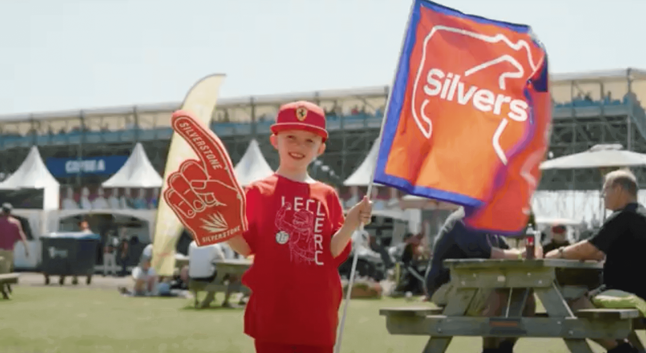Young fan in red attire holding a foam finger and flag at an outdoor event, smiling and enjoying the atmosphere.