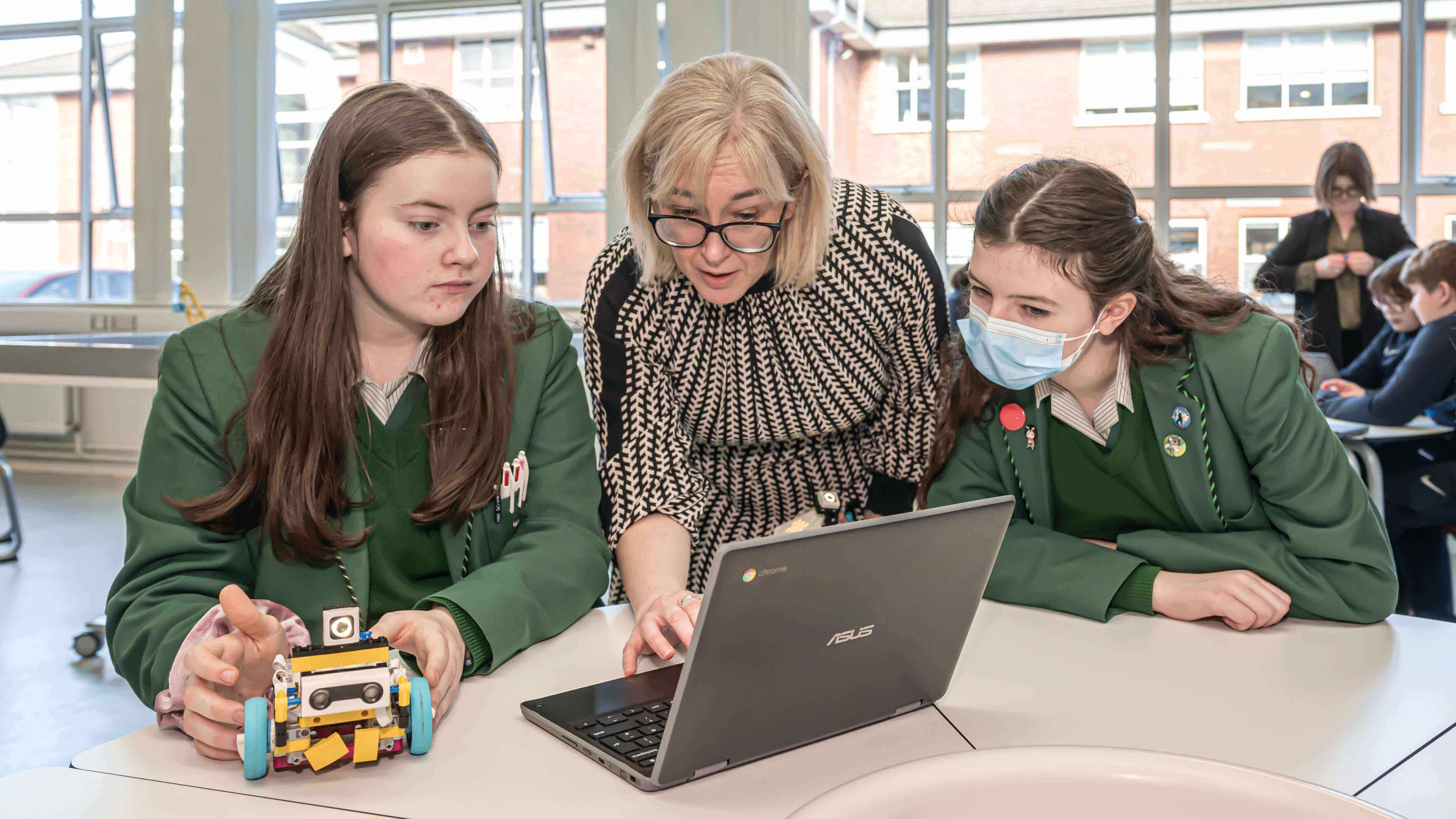Students collaborate on a robotics project with a teacher using a laptop to enhance STEM learning.