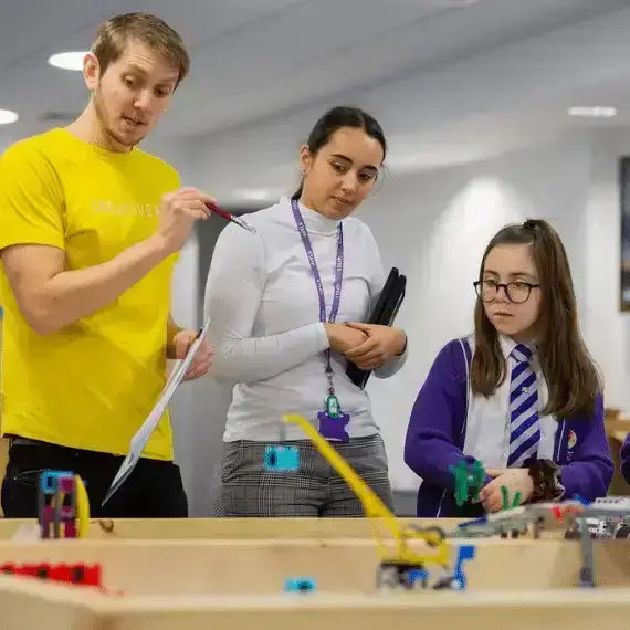 Instructor guiding students in a classroom with robotics and engineering projects, fostering hands-on learning.