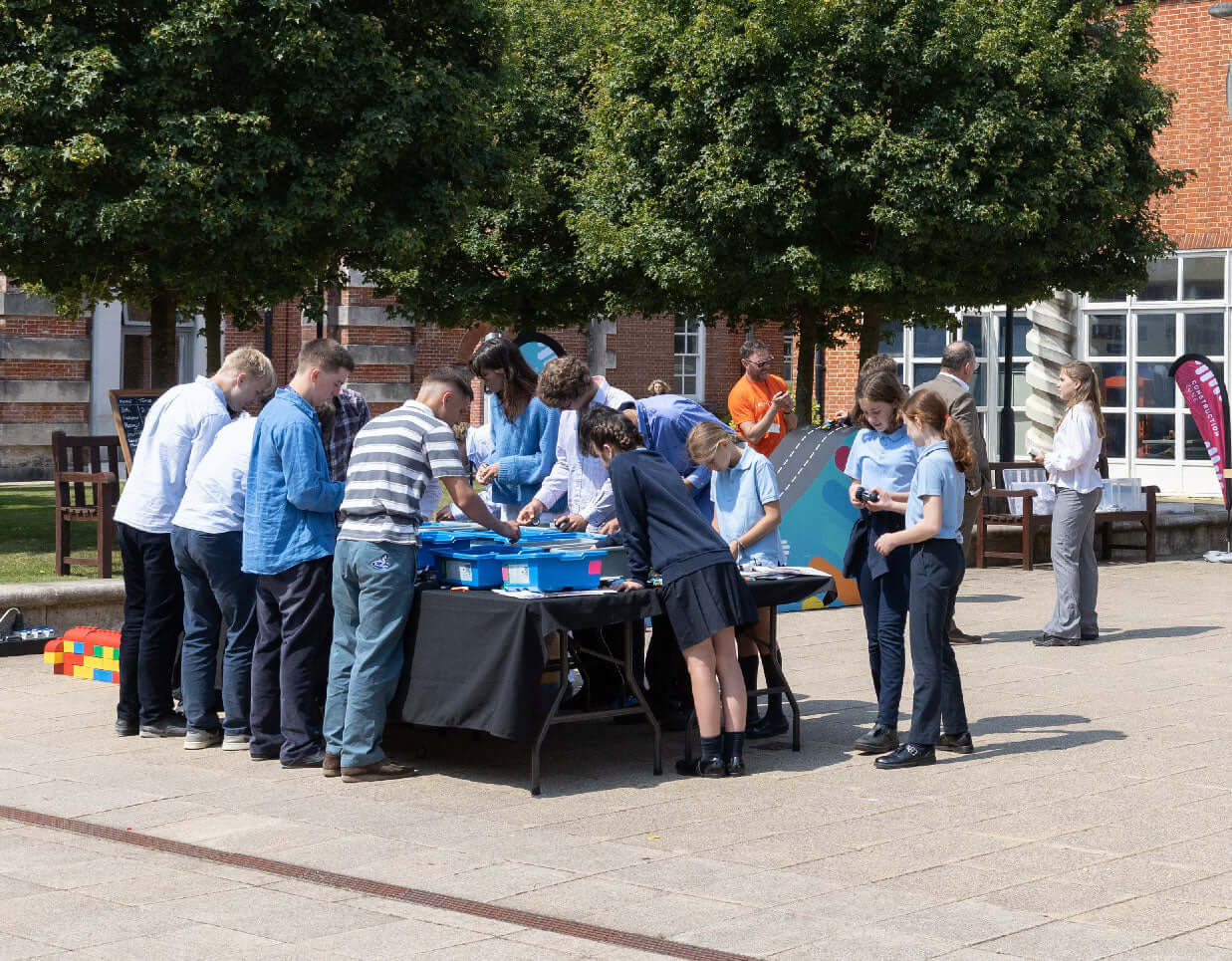 Group of people engaging in a creative activity outdoors, collaborating around a table with various tools and materials.