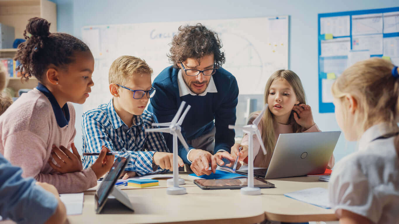 Teacher guides students in a classroom, exploring renewable energy concepts with wind turbines model.