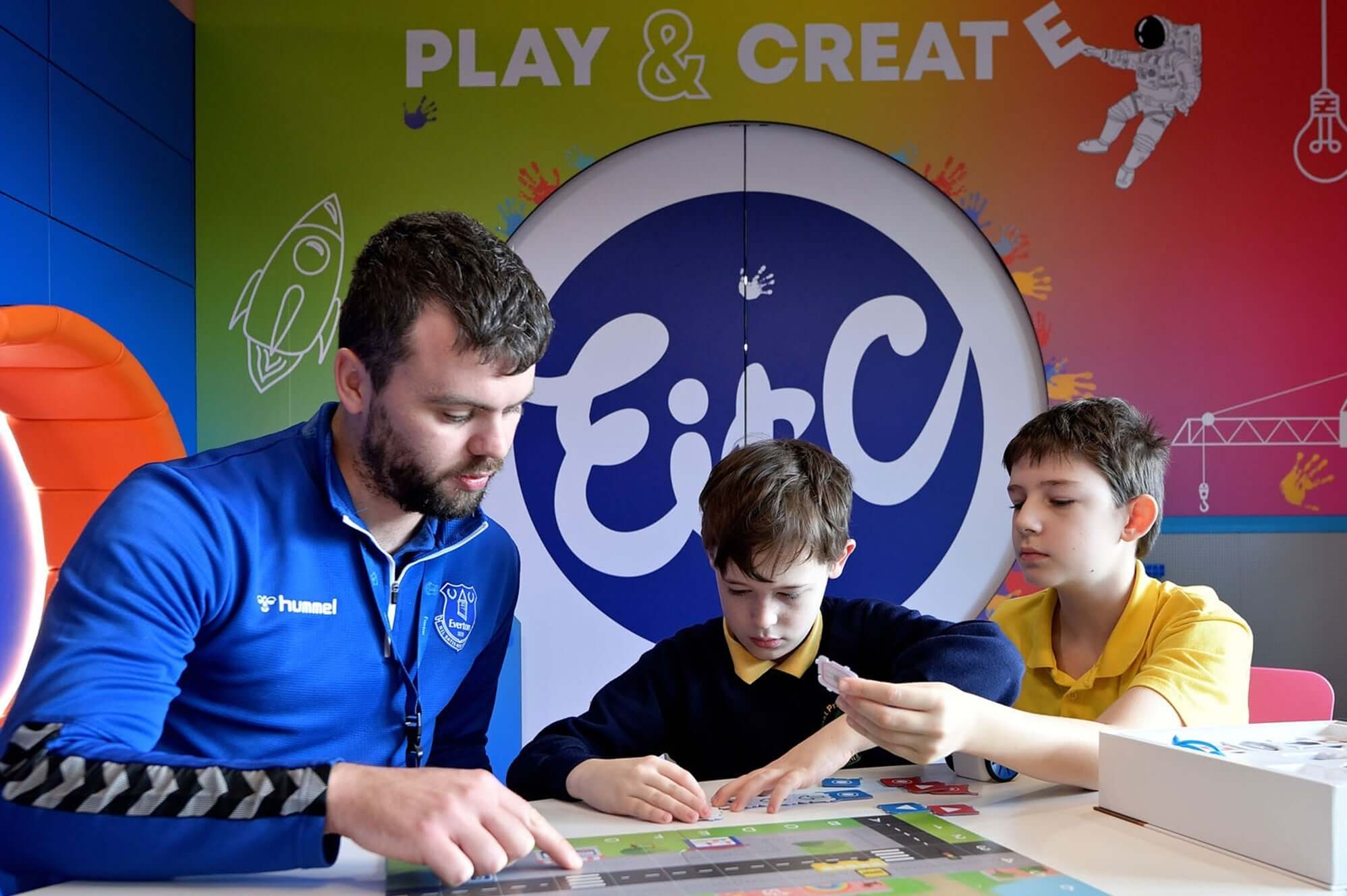 A man teaches two boys during a creative play session at a colorful educational center.