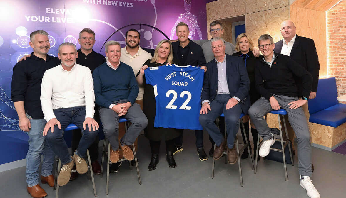 Group of professionals posing with a blue team shirt labeled 'First Team Squad 22' in an innovative office setting.
