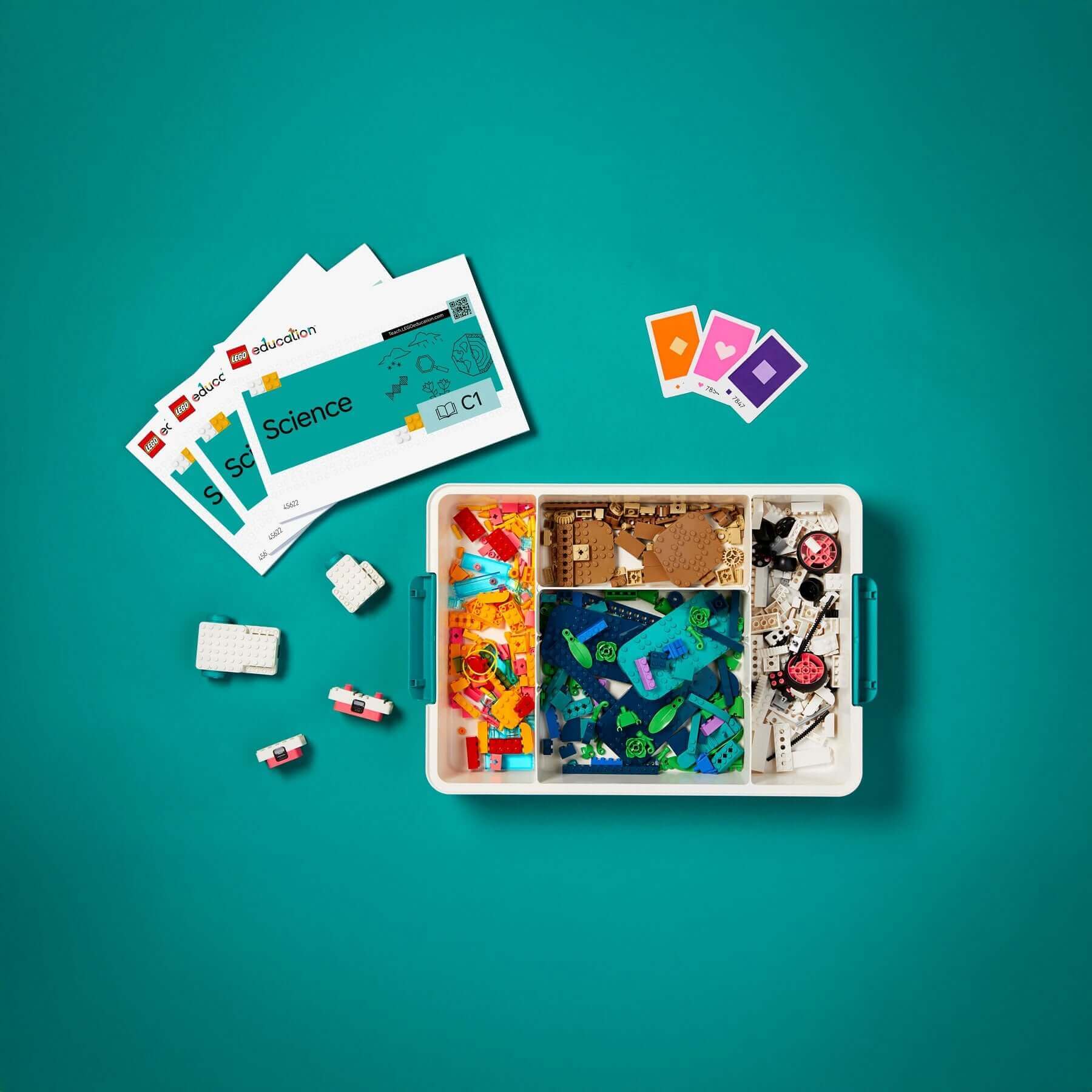 Colorful science education kit with game pieces, cards, and building materials on a teal background.