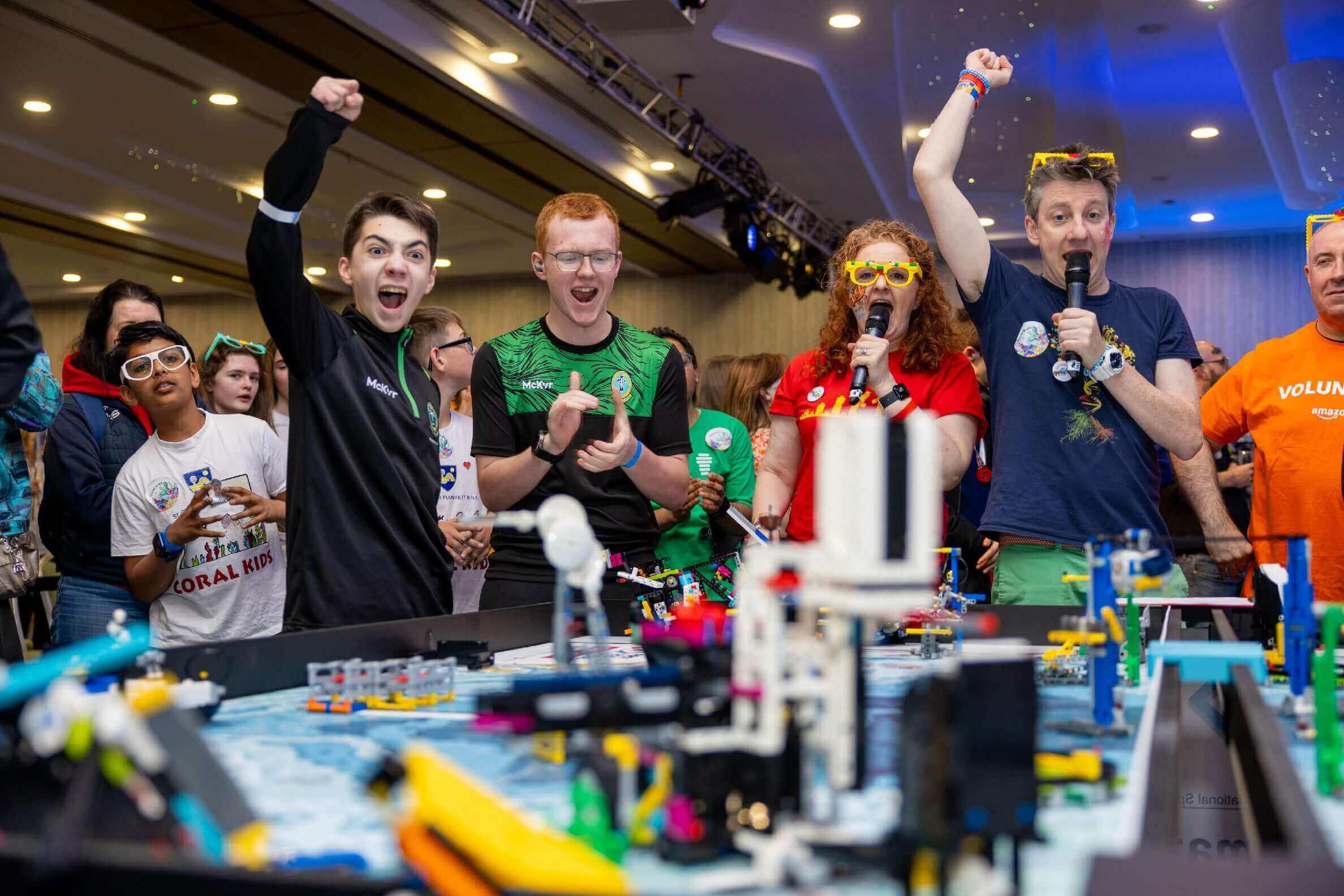 Excited participants celebrate at a robotics competition, showcasing teamwork and innovation with colorful models.