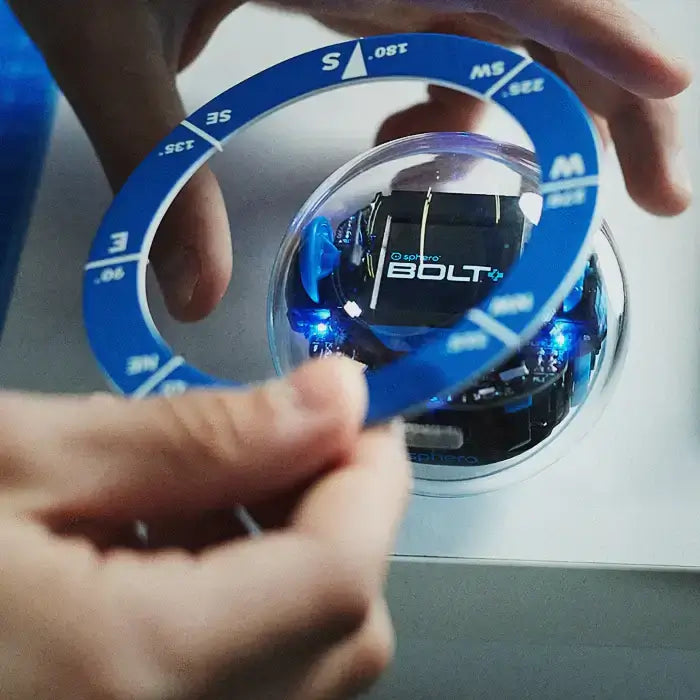 A user adjusts a blue circular guide on a Sphero BOLT robot, showcasing its programmable features and LED lights.