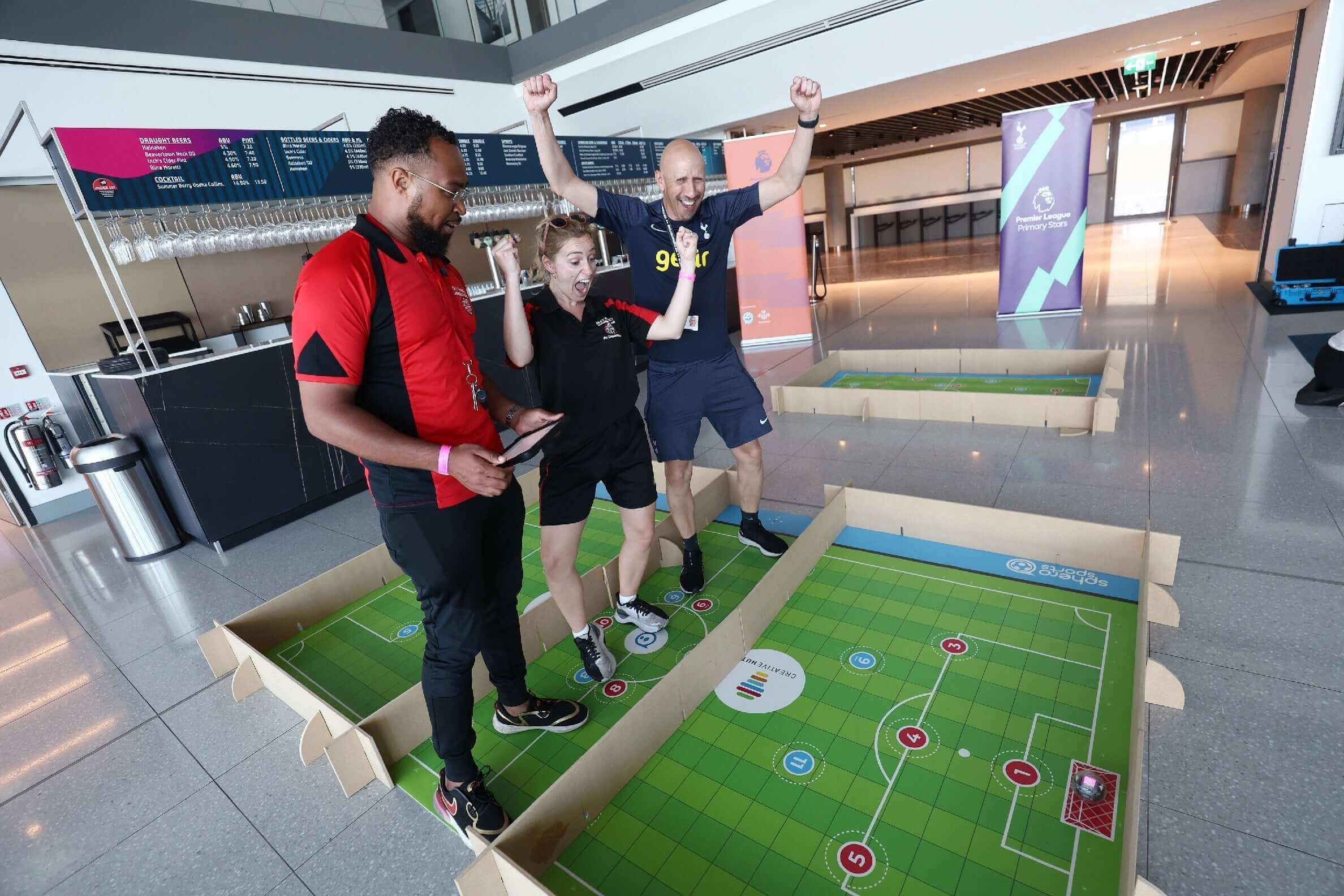 Three people enjoy a game on a large sports-themed board, celebrating in a modern indoor space.
