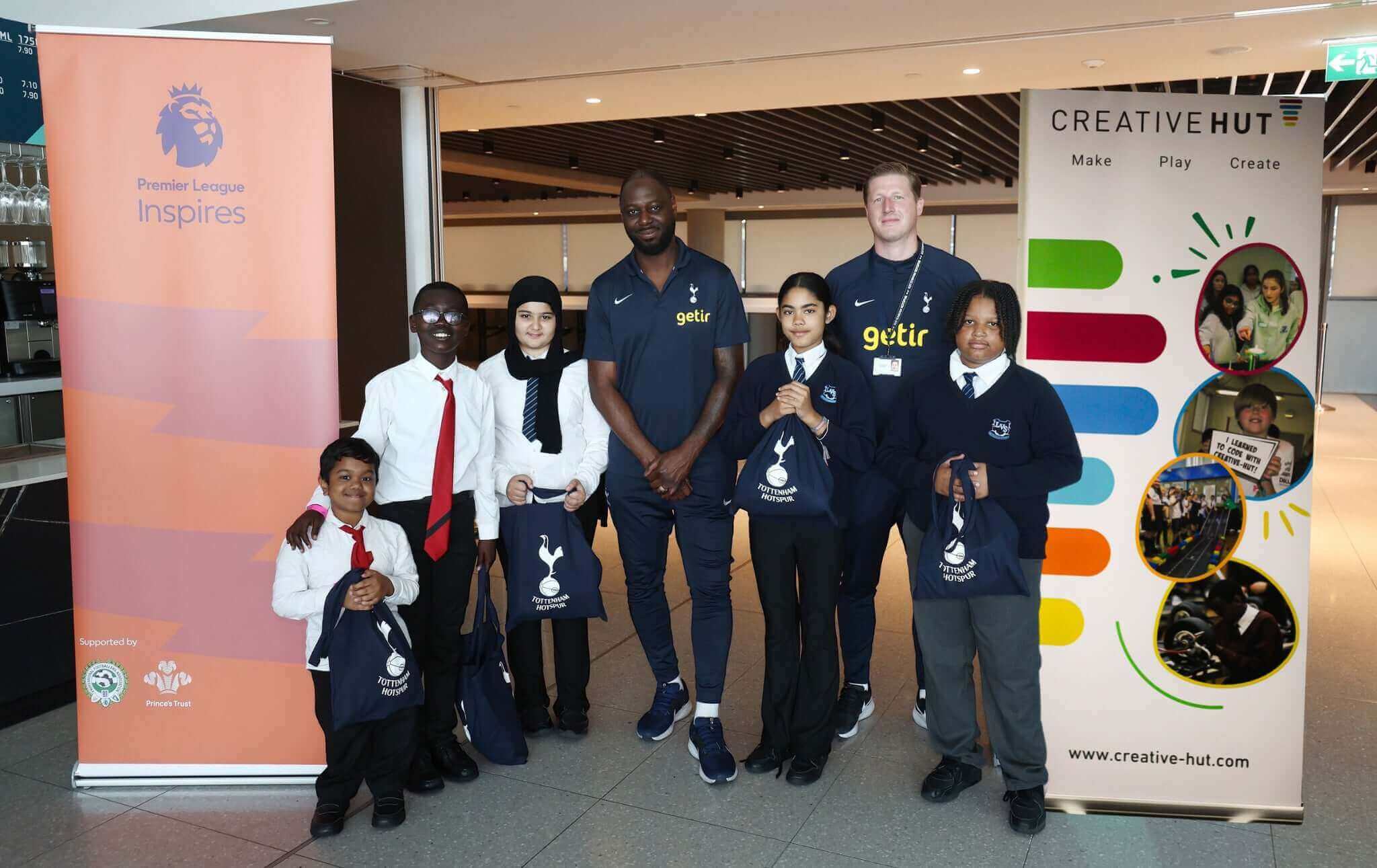 A group of children and mentors pose with bags at a Premier Language event, showcasing creativity and teamwork.