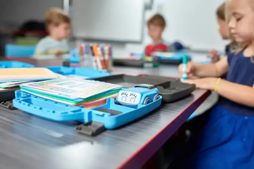 Kids engaged in creative learning with colorful supplies and a blue tech device in a classroom setting.