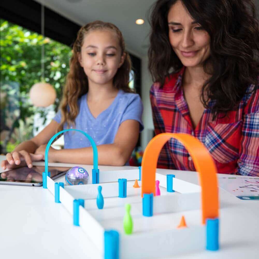 Mom and daughter play with a colorful, interactive toy on a table, showcasing creativity and fun in a bright room.