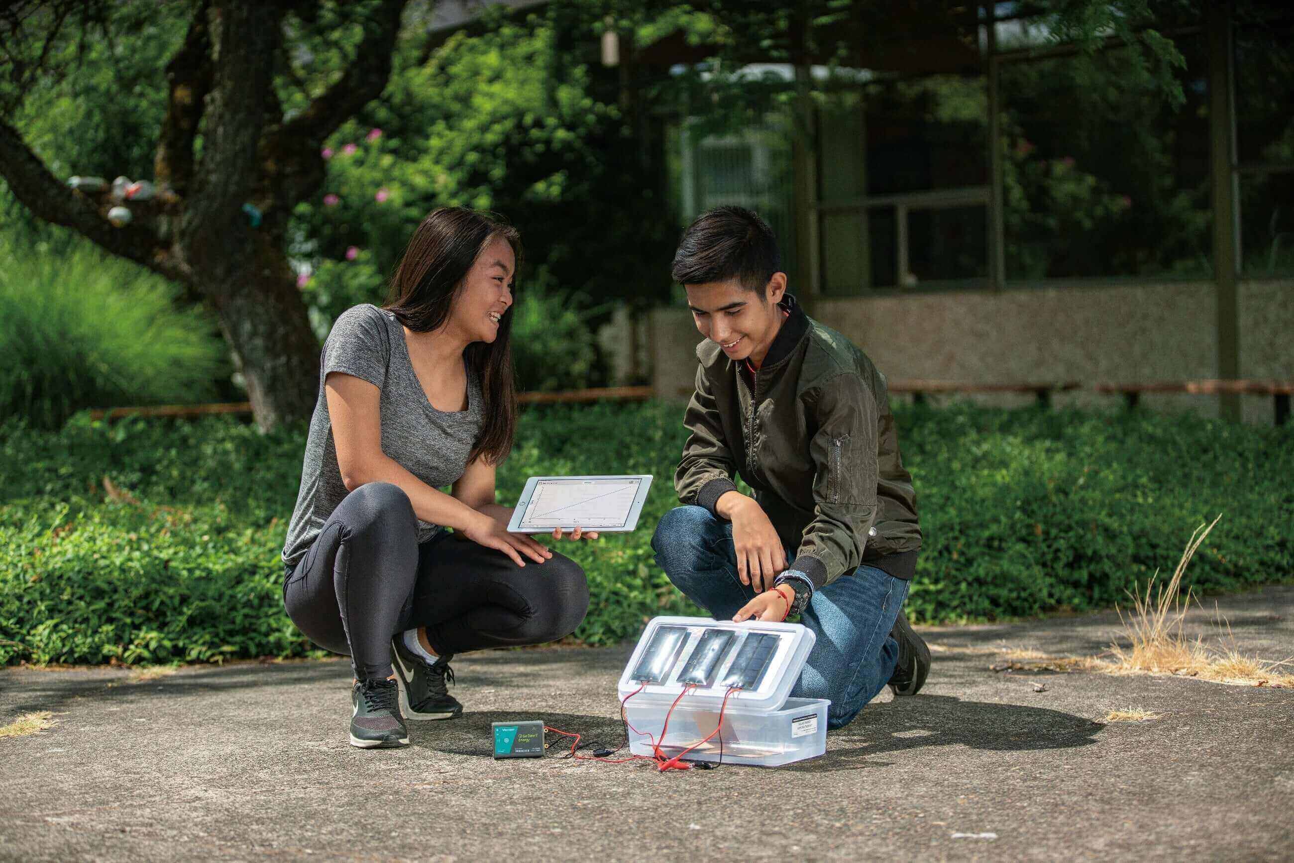 Students demonstrating a solar energy project outdoors, using a tablet and solar panel setup.
