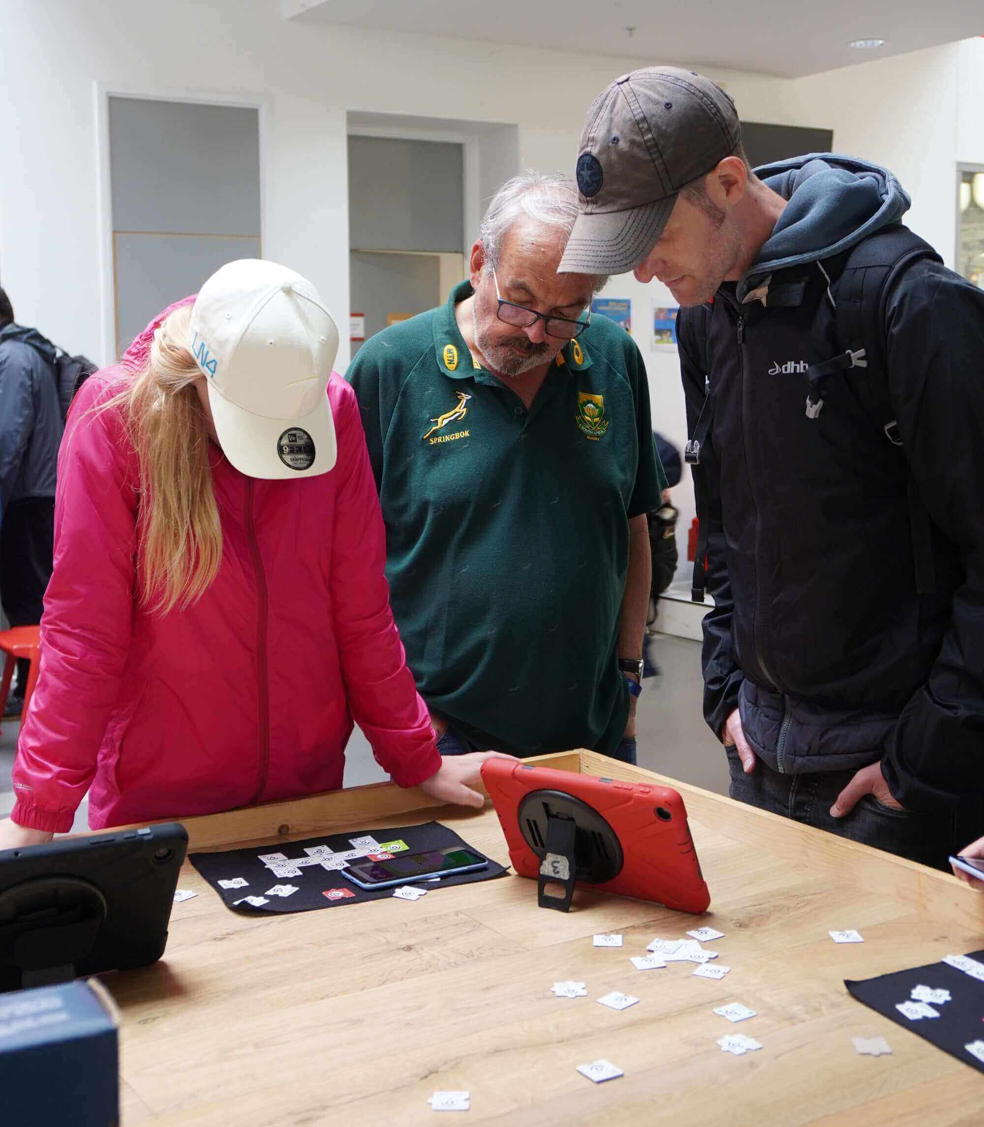 Three individuals engaged in a learning activity, examining a tablet and puzzle pieces on a table.