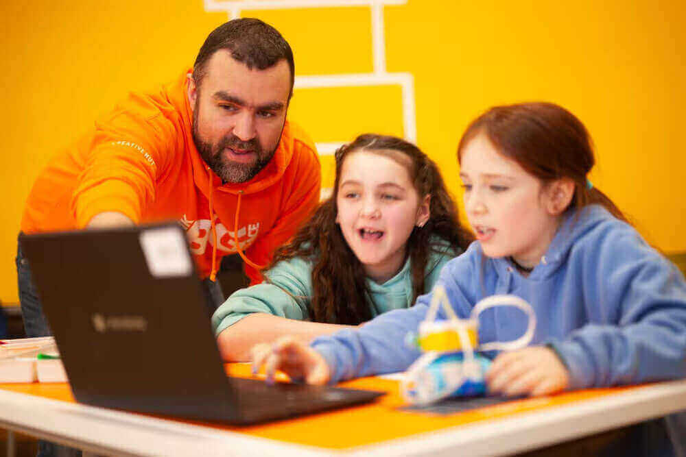 Instructor guiding two girls in a learning session using a laptop, showcasing interactive education.
