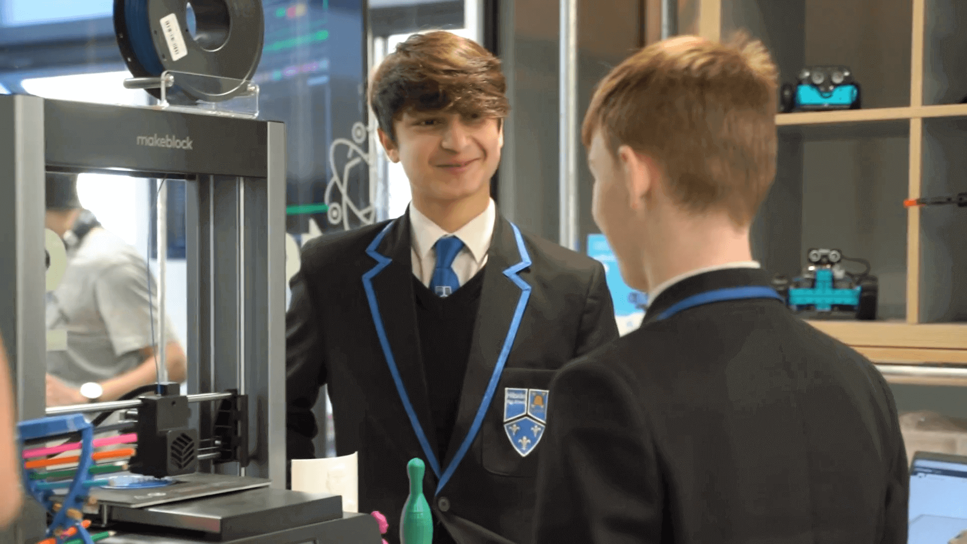 Students in school uniforms interacting in a tech lab with a 3D printer, showcasing hands-on learning and creativity.