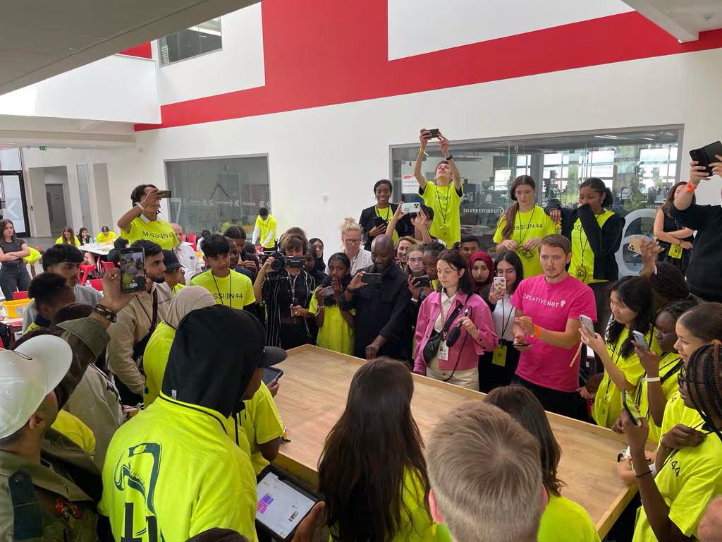 Group of diverse youth in bright yellow shirts engaging in a collaborative tech event, with excitement and enthusiasm.