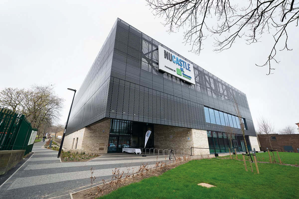 Modern Newcastle building with distinctive black mesh facade and prominent signage, surrounded by greenery.