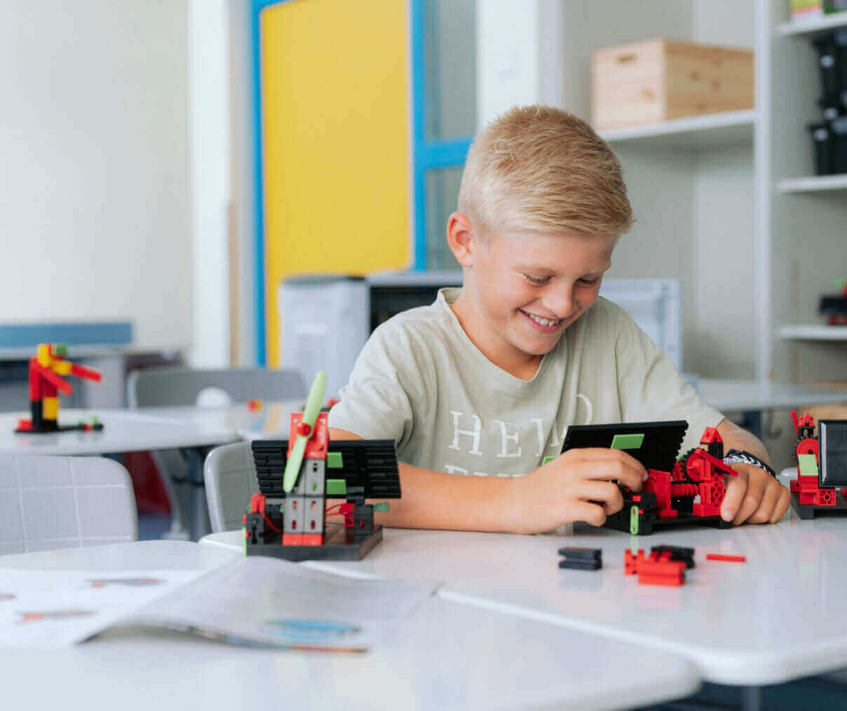 Smiling boy building with LEGO blocks in a bright classroom, showcasing hands-on learning and creativity.