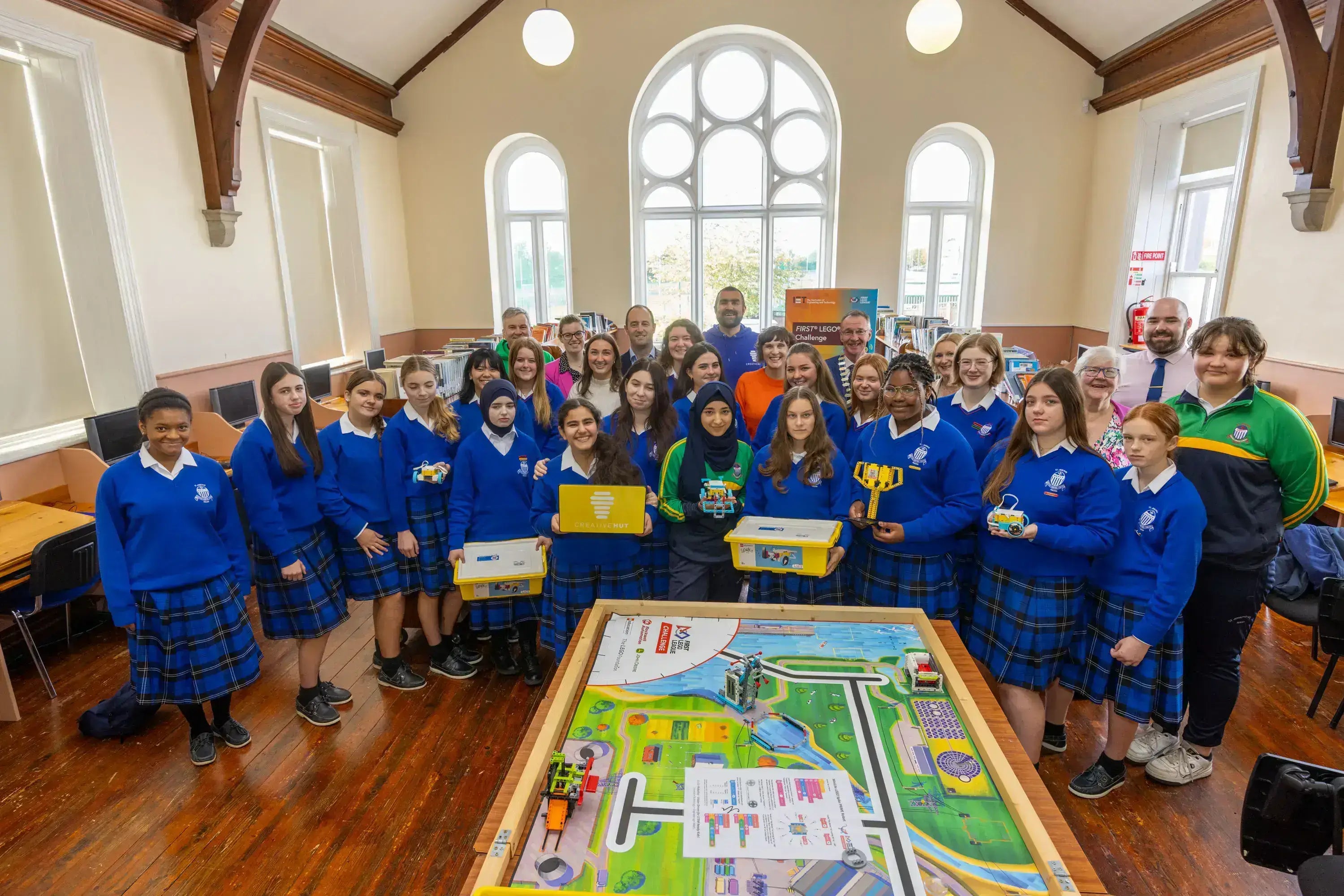 Group of students in blue uniforms gathered around a learning table, promoting education and teamwork in a bright classroom.