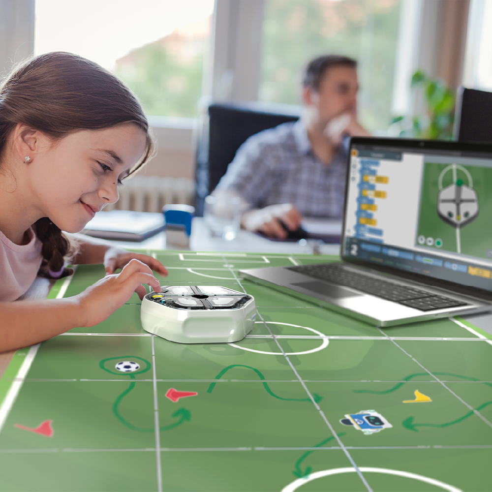 Young girl programming a robotic soccer player with a laptop on a gaming mat, demonstrating interactive learning.