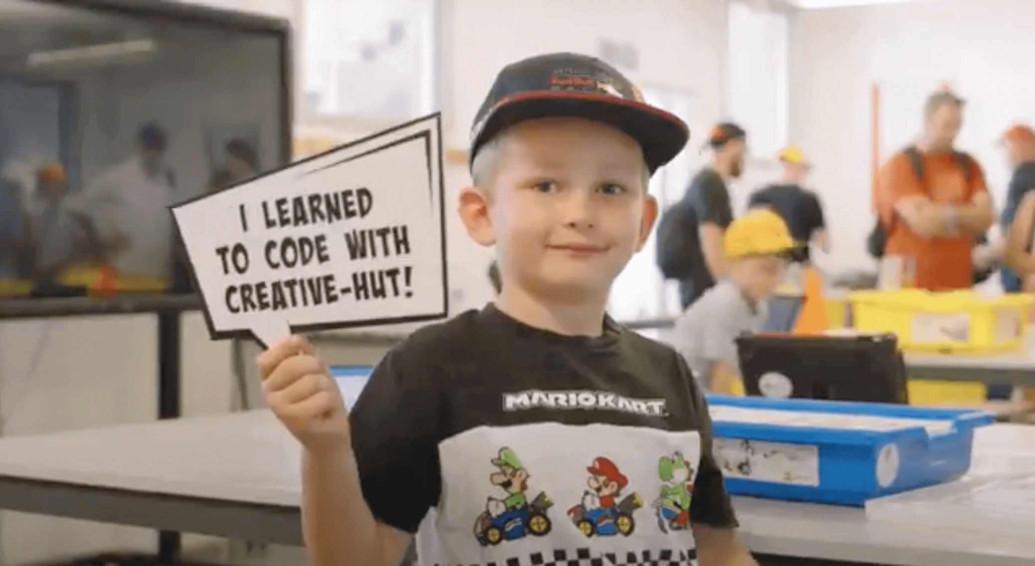 Young boy holding a sign that says 'I learned to code with Creative-Hut!' in a coding workshop.