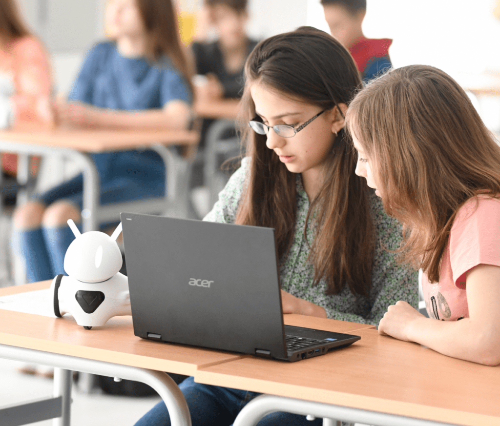 Two students collaborating with a laptop and a robot in a classroom setting.