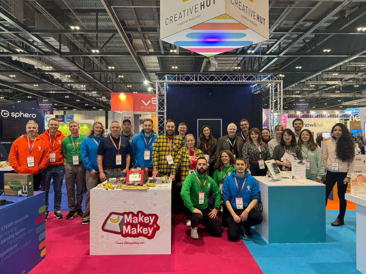 Group photo of attendees at Creative Hut event featuring the Makey Makey booth and colorful event backdrop.