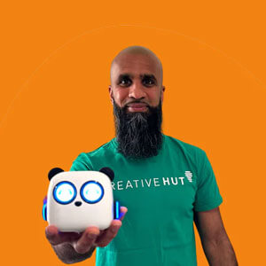 A man with a beard wearing a green t-shirt holding a small robot toy against an orange background.