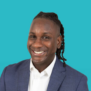 Portrait of a smiling man in a blue suit against a bright teal background, exuding confidence and professionalism.