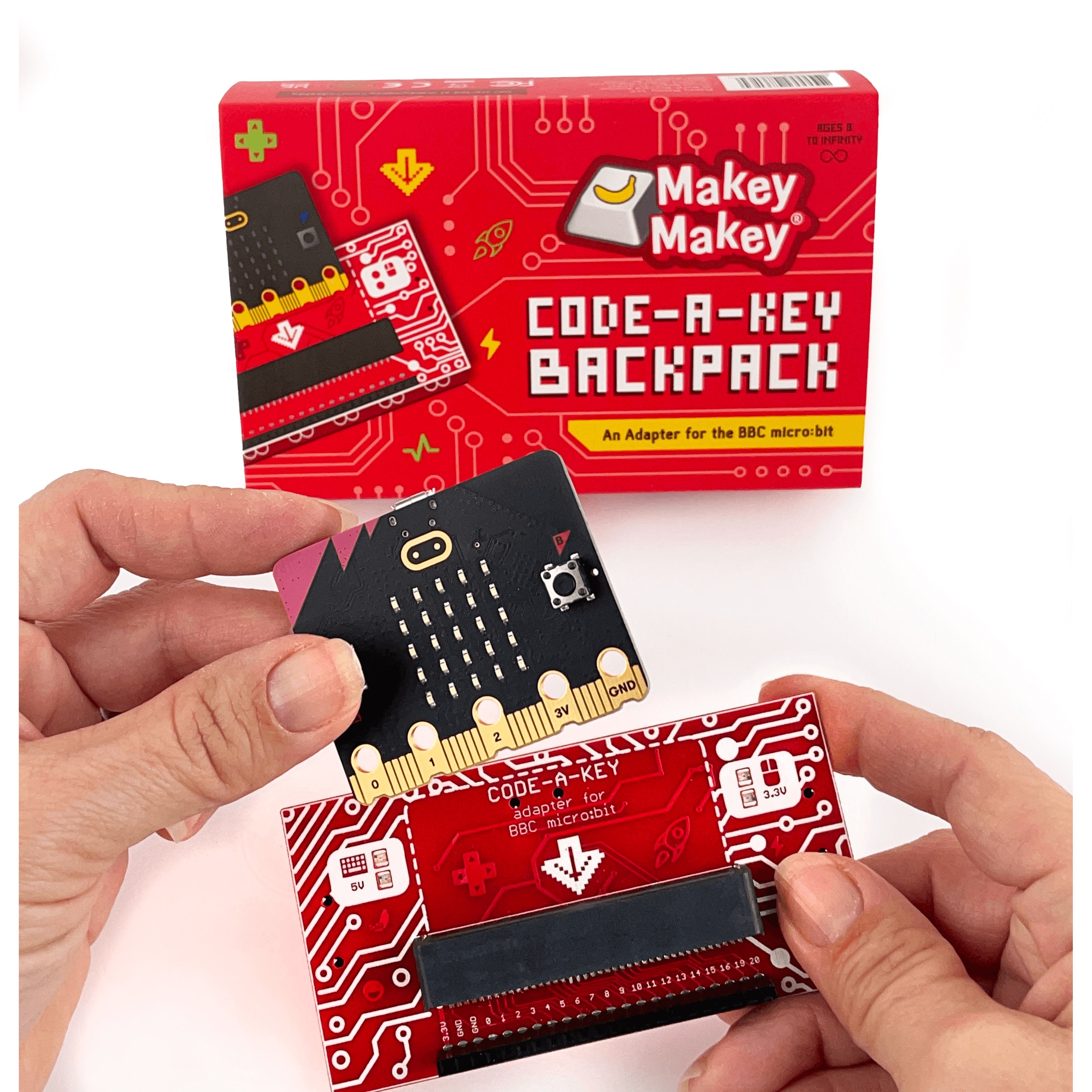 Hands holding Makey Makey Code-a-Key Backpack adapter for BBC micro:bit with packaging in the background.