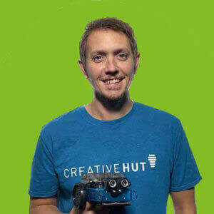 Smiling man in blue Creative Hut shirt holding a remote-controlled car against a bright green background.