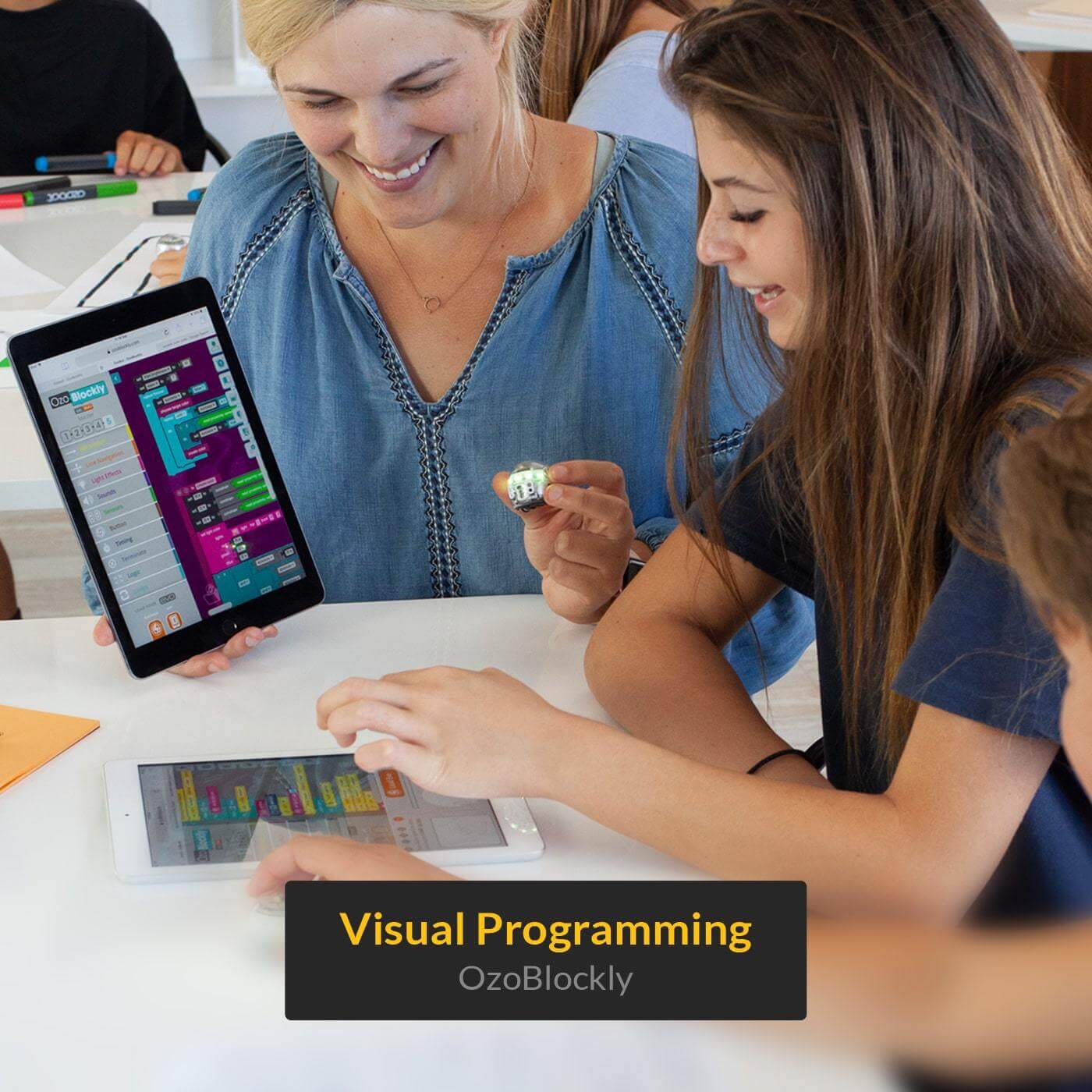 Students engaged in visual programming with Ozobot Evo using tablets and Blockly interface in a classroom setting.