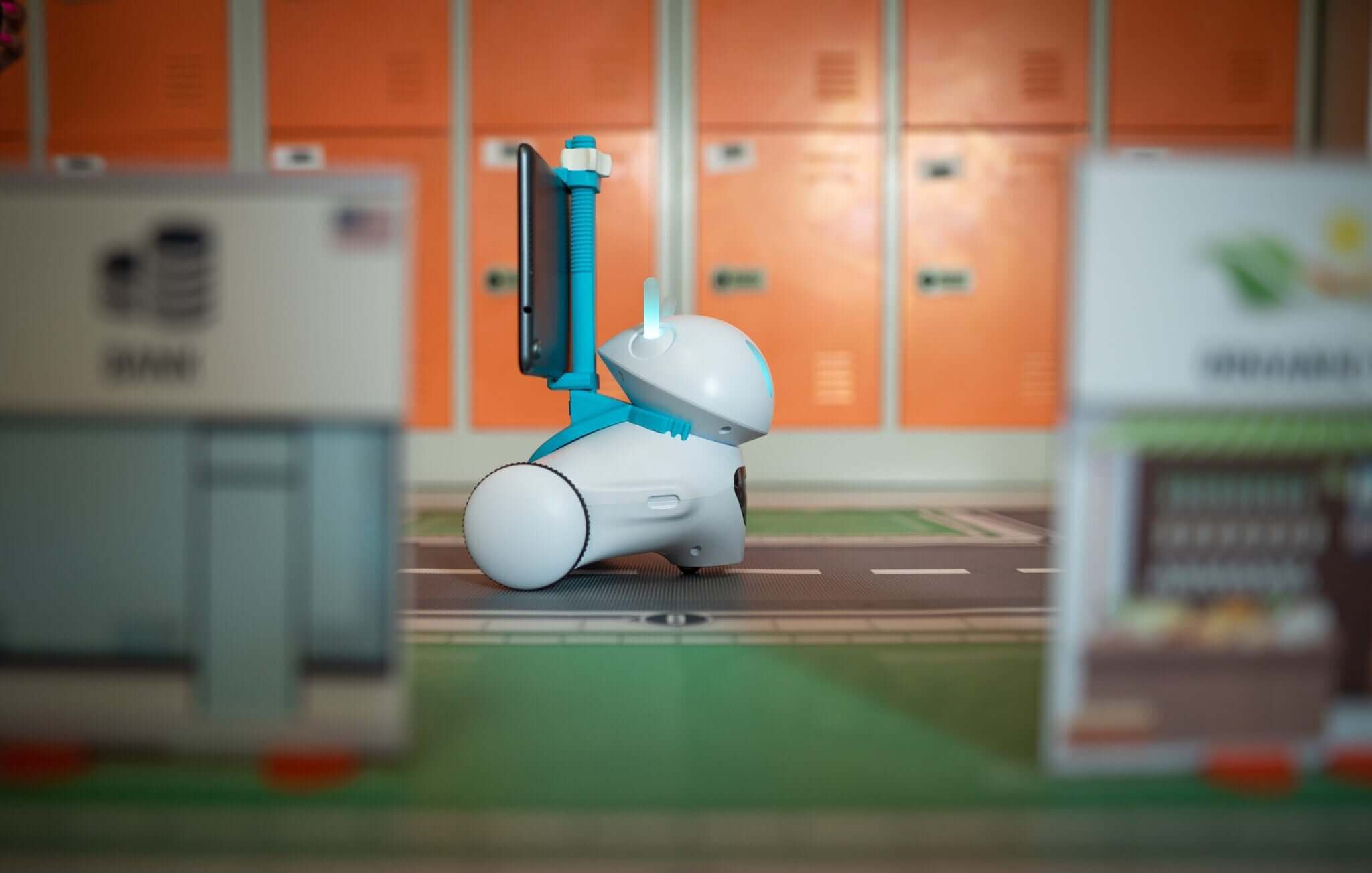 A small, robotic device on a miniature road with orange lockers in the background, showcasing technology in a playful setup.