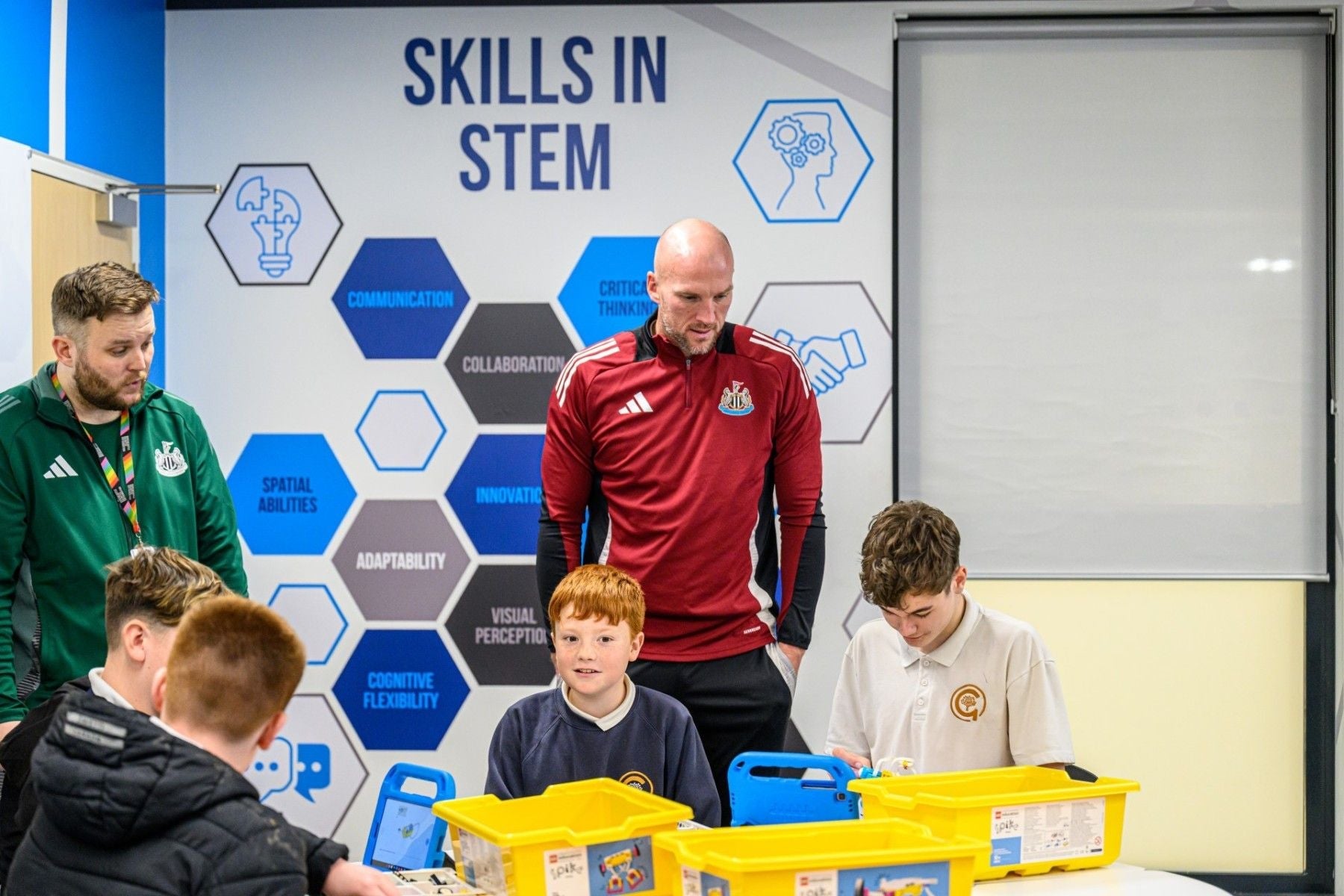 Coaches interact with children during a STEM skills workshop, showcasing engagement and learning in a classroom setting.